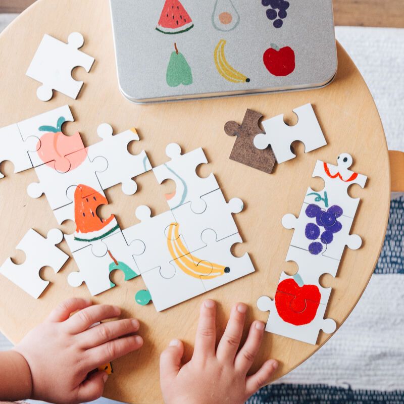 Child solving a 30-piece personalized jigsaw puzzle from Piecemakers. The custom puzzle showcases a child's drawing of fruit, providing a fun and engaging activity for young puzzlers